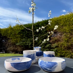 May include: Five ceramic pieces in a blue and white colour scheme. Two bowls, two small vases, and one taller vase. The pieces are sitting on a grey table.