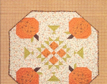 Puede incluir: Un patrón de colcha titulado "Pumpkin Party" de This & That, que presenta un diseño de patchwork con calabazas naranjas y hojas verdes sobre un fondo blanco.