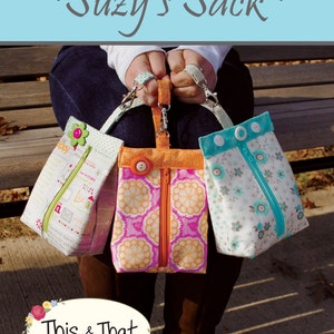 May include: Three colorful fabric bags with zippers and handles are held up. The bags have different patterns, including floral and geometric designs. The text "~ Suzy's Sack ~" is at the top, and "This & That" is at the bottom.