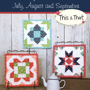 May include: Three small quilt blocks, each with a different design, are displayed on a wooden surface. The blocks are red, white, blue, and green. The blocks are titled "Bitty Barn Blocks" and "This & That".