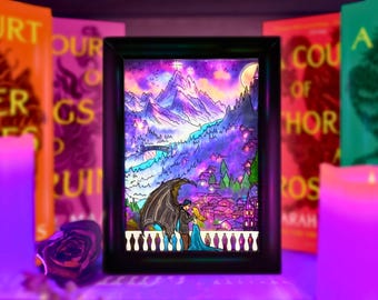 Può includere: Una cornice nera rettangolare contenente un'illustrazione retroilluminata di una coppia su un balcone. La scena mostra una figura alata e una persona con un abito blu su uno sfondo di montagne viola, un ponte e un villaggio sotto un cielo al chiaro di luna.