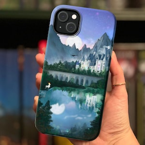 以下が含まれることがあります： 城と月が描かれた青と紫のグラデーションの背景を持つ携帯電話ケース。ケースには黒いカメラの切り抜きと白いユニコーンのシルエットがあります。