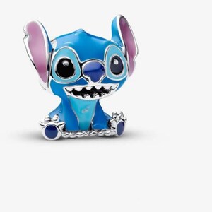 May include: A blue and silver charm featuring the character Stitch from the Disney movie Lilo & Stitch. The charm has large black eyes, a wide grin, and large ears with pink inner details. The charm is made of metal and enamel.