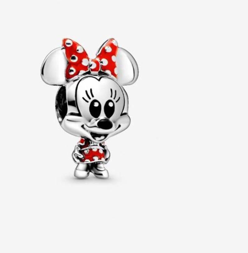 May include: A silver charm featuring Minnie Mouse. The charm has a red bow with white polka dots, a red dress with white polka dots, and black eyes. The charm is a three-dimensional design.