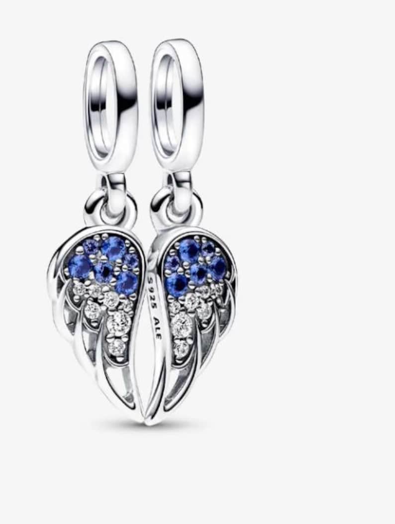 May include: A pair of silver-colored dangle earrings, each shaped like a wing. The wings are adorned with blue and clear gemstones. The earrings have a loop at the top for hanging.