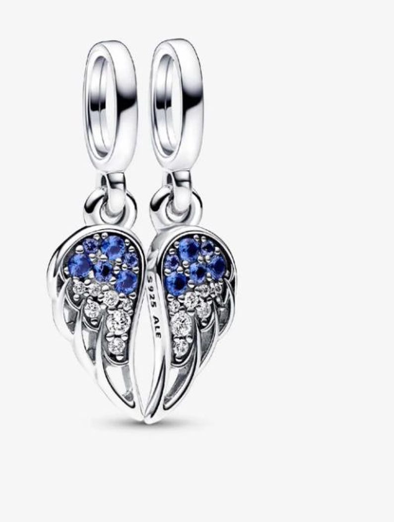 May include: A pair of silver-colored dangle earrings, each shaped like a wing. The wings are adorned with blue and clear gemstones. The earrings have a loop at the top for hanging.