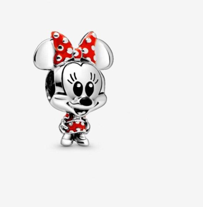 May include: A silver charm featuring Minnie Mouse. The charm has a red bow with white polka dots, a red dress with white polka dots, and black eyes. The charm is a three-dimensional design.