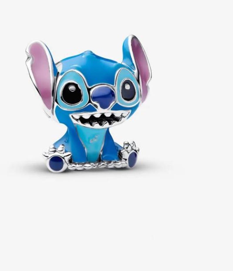 May include: A blue and silver charm featuring the character Stitch from the Disney movie Lilo & Stitch. The charm has large black eyes, a wide grin, and large ears with pink inner details. The charm is made of metal and enamel.