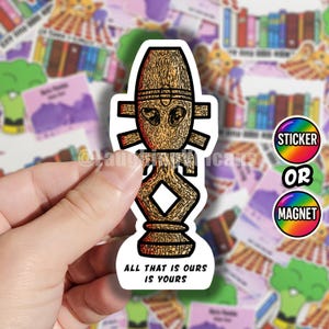 May include: A die-cut sticker featuring a brown, textured, stylised wooden figure with a central diamond-shaped cutout and horizontal protrusions. The base of the sticker displays the black text ALL THAT IS OURS IS YOURS in a clean, sans-serif font.