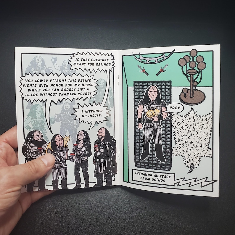Op de afbeelding: Een stripboekspread met zwart-wit illustraties en tekstballonnen. De linkerpagina toont een groep personages met tekst, terwijl de rechterpagina een personage afbeeldt dat een kat vasthoudt. Tekst bevat "Incoming message from Qo'nos."