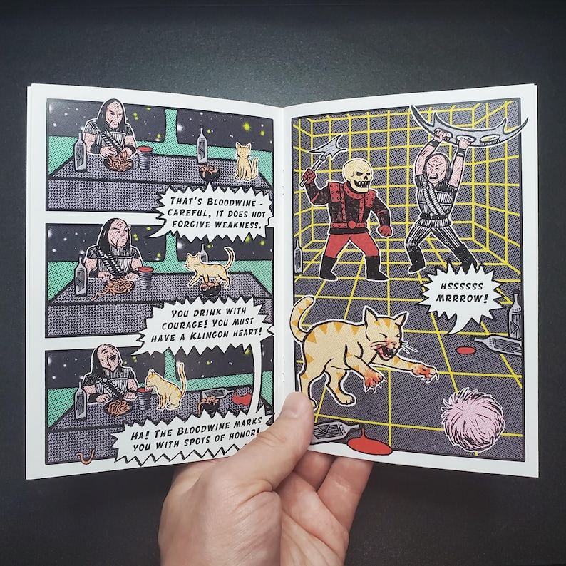 Op de afbeelding: Een stripboekpagina met illustraties van Klingons, katten en tekstballonnen. De illustraties zijn in retrostijl met een rasterachtergrond. De tekst bevat zinnen als "That's Bloodwine" en "Hssssss Mrrrow!"