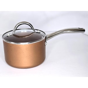 May include: A copper-coloured saucepan with a clear glass lid and a stainless steel handle. The handle is curved and attached to the side of the pan. The lid has a stainless steel handle. The pan is on a white surface.