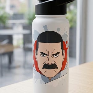 May include: White water bottle with a black lid featuring a cartoon illustration of a man with a mustache. The design includes a red and gray splatter effect around the face. The bottle is on a wooden surface.