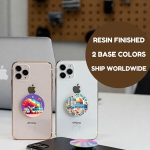 Op de afbeelding: Twee iPhone-hoesjes met kleurrijke telefoonbeugels. De beugels hebben een moskee-ontwerp. De tekst "RESIN FINISHED", "2 BASE COLORS" en "SHIP WORLDWIDE" is zichtbaar op de achtergrond.