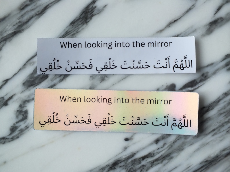 May include: Two white rectangular stickers with black text. The top sticker has the text "When looking into the mirror" and the Arabic text "اللَّهُمَّ أَنْتَ حَسَّنْتَ خَلْقِي فَحَسِّنْ خُلُقِي". The bottom sticker has the same text but is on a holographic background.
