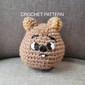 May include: Crochet pattern for a brown amigurumi animal with black eyes, a black nose, and a white tooth. The animal has large, floppy ears with a yellow accent.