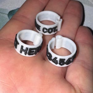 May include: Three white plastic rings with black text. One ring reads "E COT", another reads "IT HER", and the third reads "3456". The rings are designed to be clipped together.