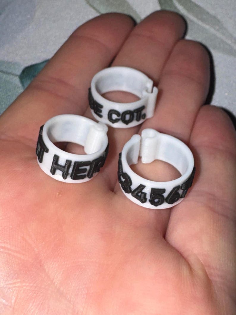 May include: Three white plastic rings with black text. One ring reads "E COT", another reads "IT HER", and the third reads "3456". The rings are designed to be clipped together.