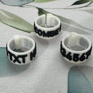 May include: Three white rings with black text and numbers. One ring reads "COMBE!", another "TXT H", and the third displays "34567". The rings are likely for identification or organization.