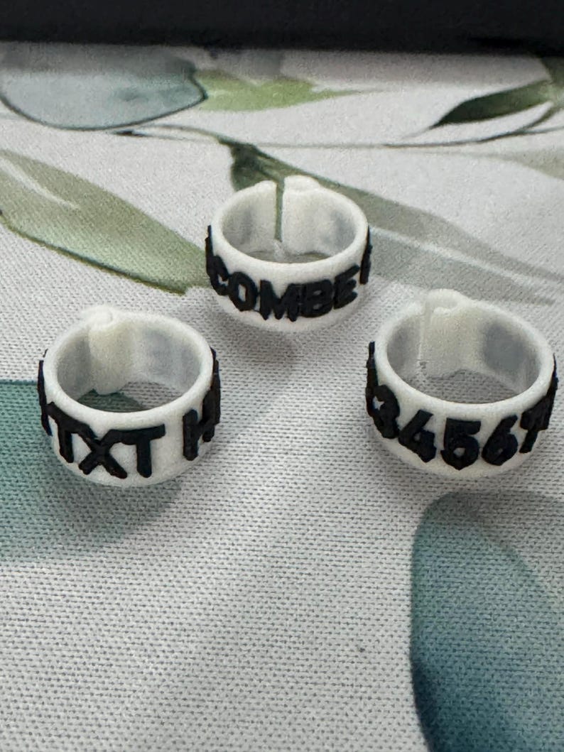 May include: Three white rings with black text and numbers. One ring reads "COMBE!", another "TXT H", and the third displays "34567". The rings are likely for identification or organization.