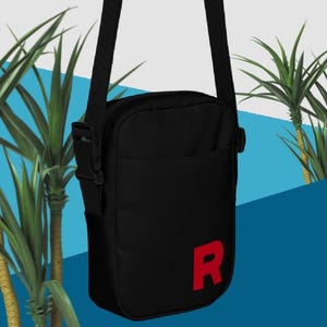 May include: A black shoulder bag with a red "R" on the front. The bag has a zip closure and an adjustable strap.