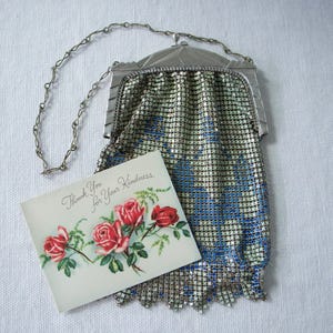 May include: A silver-toned metal mesh handbag with a blue floral pattern, featuring a hinged frame and a delicate chain strap, displayed alongside a rectangular card with red roses and the text Thank You for Your Kindness.