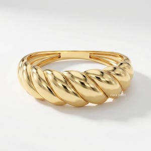 May include: A gold-colored ring with a twisted design. The ring has a smooth, polished surface and a rounded shape. The ring is a piece of jewelry.