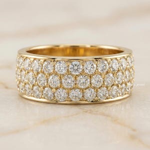 Op de afbeelding: Een brede, gouden bandring met drie rijen sprankelende, rond geslepen diamanten. De ring heeft een gepolijste, geelgouden afwerking. De ring is een sieraad.