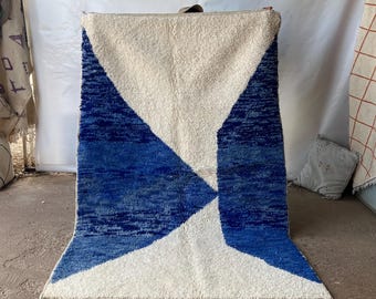 May include: A white and blue geometric rug with a modern design. The rug has a fringe border and is made of a soft, plush material.
