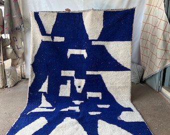 May include: A white and blue abstract rug with a geometric design. The rug has a fringe border.