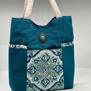 Può includere: Una borsa tote blu turchese con una tasca in tessuto a fantasia e un abbellimento in pietra turchese.