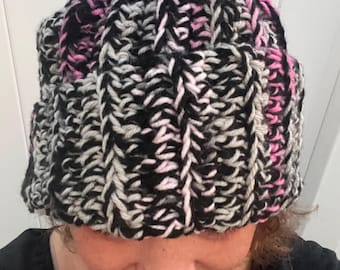 May include: A black, gray, and pink knitted beanie hat. The hat has a cable knit pattern.
