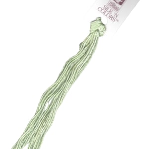 Może przedstawiać: Sznurek do haftu w jasnozielonym kolorze z białą metką z napisem "SILK 'N COLORS™" i małą ilustracją kobiety.