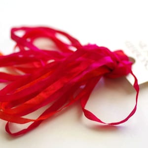 May include: A bundle of vibrant red and fuchsia silk ribbons, tied together with a tag. The ribbons are thin and flowing, with a slight sheen. The tag has text, but it is too blurry to read.
