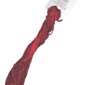 Op de afbeelding: Een spoel met dieprode zijden chenille borduurgaren met een wit label waarop "DMC SILKEN CHENILLE" staat.