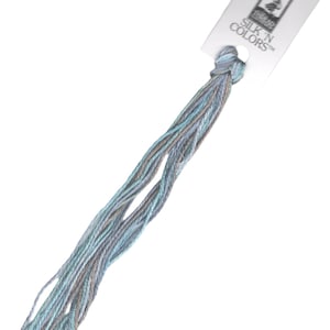 Può includere: Un gomitolo di filo da ricamo di colore azzurro chiaro, grigio e beige con un'etichetta bianca su cui è scritto "SILK 'N COLORS™".