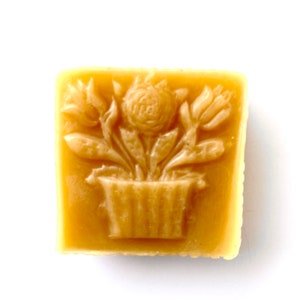 May include: A square block of beeswax with a raised design of a flower pot with three flowers in it.