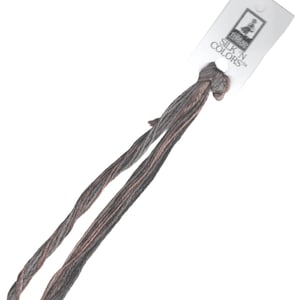 Op de afbeelding: Een klosje grijs en bruin borduurgaren met een wit etiket waarop "SILK 'N COLORS™" staat en een kleine afbeelding van een vrouw met een naald en draad.