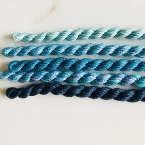 Puede incluir: Seis madejas de hilo de bordar en tonos de azul, de claro a oscuro.