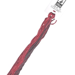 Puede incluir: Un ovillo de hilo de bordar rojo y gris con una etiqueta blanca que dice "SILK 'N COLORS" y una pequeña imagen de una mujer con un vestido.