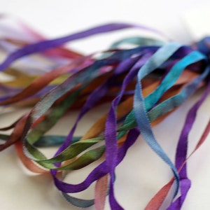 May include: A bundle of colorful silk ribbon in shades of purple, blue, green, and brown. The ribbon is hand-dyed and has a gradient effect.