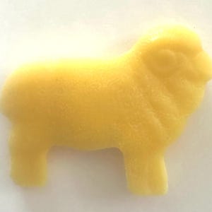 May include: A solid yellow sheep figurine. The sheep is in a side profile, with a textured surface. The figurine has four legs, a rounded body, and a detailed head with visible eyes and ears. The background is white.