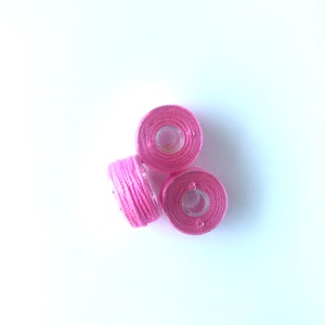Può includere: Tre bobine di filo rosa, ciascuna con un centro in plastica trasparente.