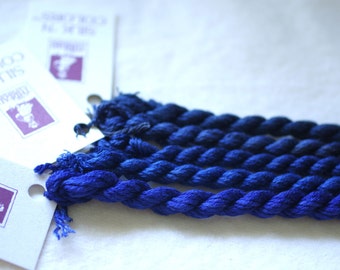 May include: A collection of six skeins of blue silk embroidery floss. The floss is arranged in a fan shape and is ready for use in a craft project.