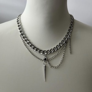 May include: A silver layered chain necklace with a small black bead and a silver spike pendant.