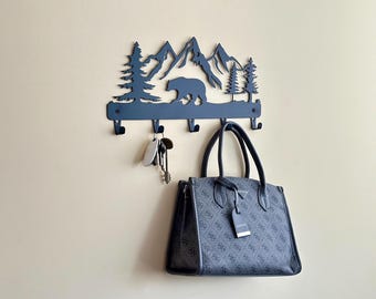 Könnte beinhalten: Schwarzer Wand-Schlüsselhalter aus Metall mit einer Silhouette von Bergen, Bäumen und einem Bären. Der Halter hat fünf Haken und eine Handtasche hängt an einem der Haken.