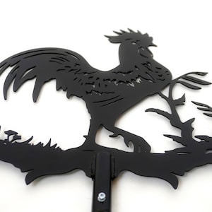 Pode incluir: Silhueta de metal preto de um galo em p&eacute; em um galho com um design detalhado. O galo est&aacute; virado para a direita e tem uma cauda longa. A silhueta &eacute; montada em uma haste de metal preto.