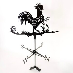 Pode incluir: Catavento de metal preto em forma de galo com uma rosa dos ventos e uma flecha. O galo est&aacute; empoleirado em um galho com folhas.