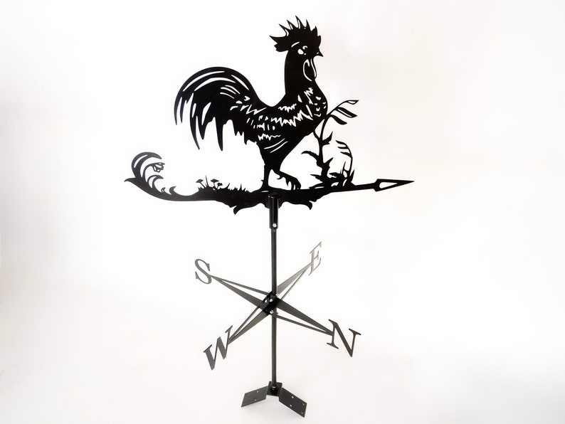 Pode incluir: Catavento de metal preto em forma de galo com uma rosa dos ventos e uma flecha. O galo est&aacute; empoleirado em um galho com folhas.