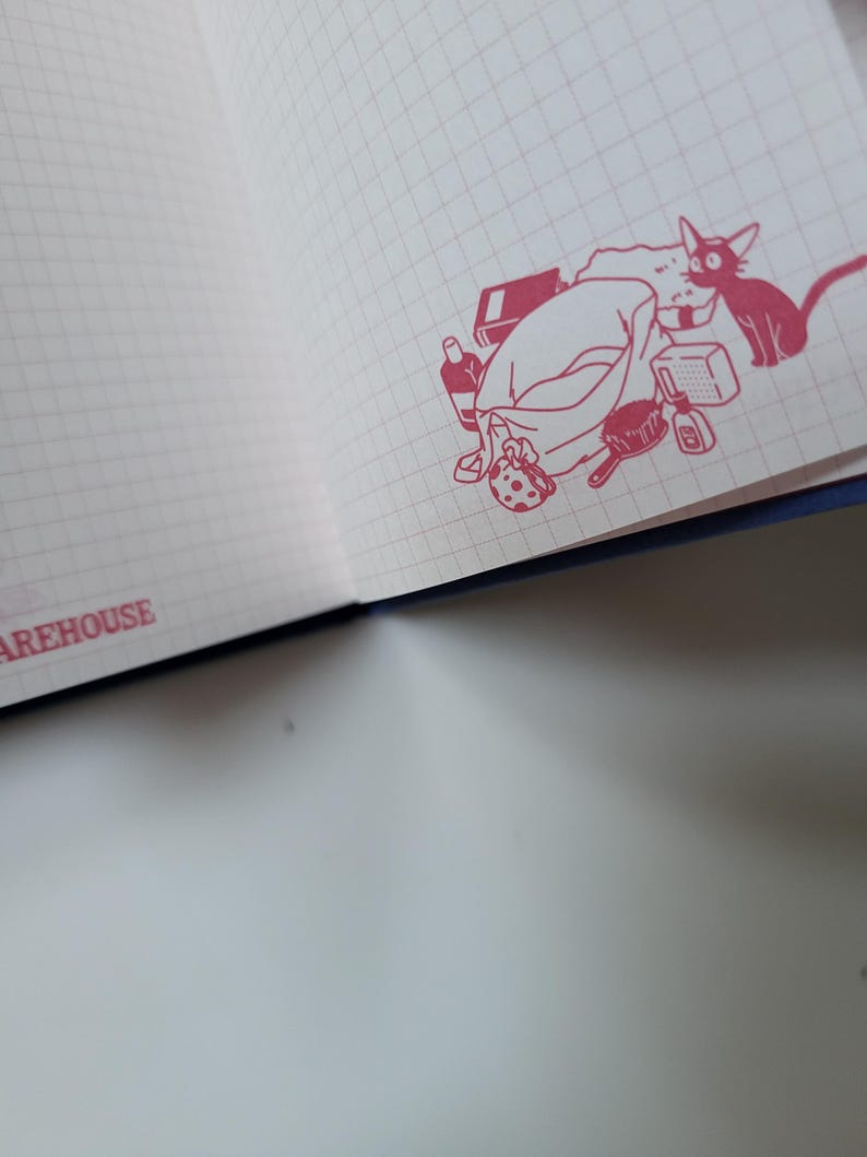 May include: Open notebook with a grid pattern on the pages. A red illustration of a cat and a pile of items, including a bag, bottle, and brush, is in the corner. The word "WAREHOUSE" is printed in red along the edge.